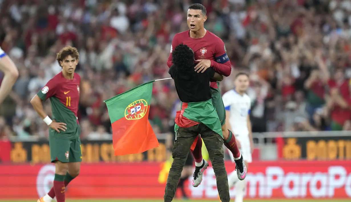 Ada momen menarik yang terjadi pada laga Kualifikasi Euro 2024 antara Portugal menghadapi Bosnia Herzegovina di Luz Stadum, Lisbon, Portugal, Minggu (18/6/2023) dini hari WIB. Di tengah laga, seorang penyusup lapangan memasuki arena pertandingan sambil mengibarkan bendera Portugal. Tak cuma berlari, pemuda berbadan kurus tersebut pun menghampiri Cristiano Ronaldo, lantas memperagakan selebrasi ikonik "siuuu" di depan sang megabintang. Bahkan sang penyusup sempat mengangkat CR-7 ke udara sebelum akhirnya ia kembali berlari menghindari kejaran petugas keamanan, hingga akhirnya ia menghentikan aksinya di pinggir lapangan sambil melakukan selebrasi "siuuu". (AP Photo/Armando Franca)