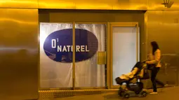 Seorang wanita mendorong kereta bayi melewati restoran nudis O'naturel yang baru dibuka di Paris, 5 Desember 2017. Sebelum makan di restoran yang hanya untuk malam hari ini, pelanggan harus menanggalkan seluruh pakaiannya. (GEOFFROY VAN DER HASSELT / AFP)
