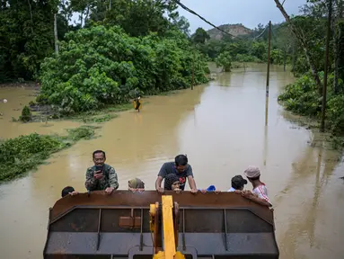 Warga terlihat dievakuasi menggunakan alat berat dari daerah di mana jalan saat ini terendam banjir di Sementeh, dekat Lanchang di negara bagian Pahang Malaysia (6/1/2021). Puluhan orang dievakuasi saat Pahang dilanda gelombang kedua banjir. (AFP/Mohd Rasfan)