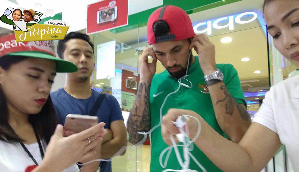 Pemain Timnas Indonesia, Stefano Lilipaly, mencoba mendengarkan suara dari telepon seluler yang diminatinya di sebuah pusat perbelanjaan di Makati City, Manila, Filipina, Minggu (20/11/2016). (Bola.com/Nicklas Hanoatubun)