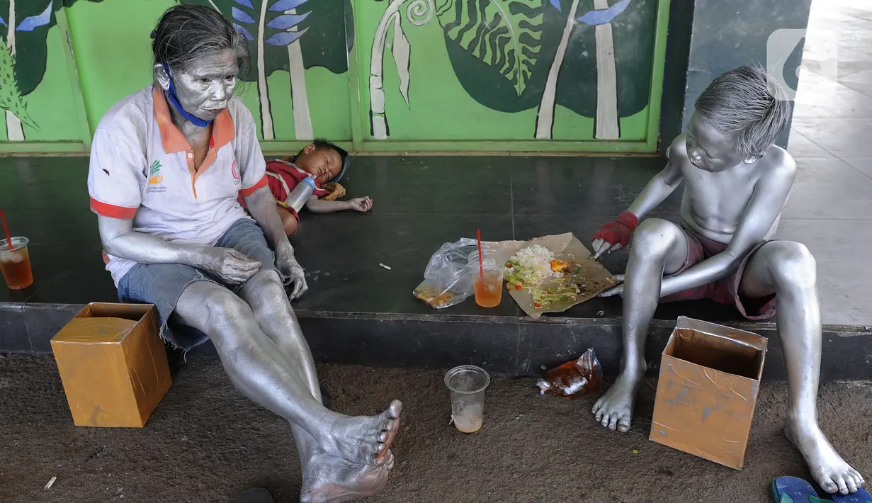 Seorang ibu bersama sang anak yang menjadi "Manusia Silver " beristirahat di salah satu sudut toko di kawasan perempatan Gaplek, Pamulang, Tangerang Selatan, Sabtu (16/1/2021). Ibu tersebut mendapat penghasilan sekitar 50 ribu per hari sebagai Manusia Silver (merdeka.com/Arie Basuki)