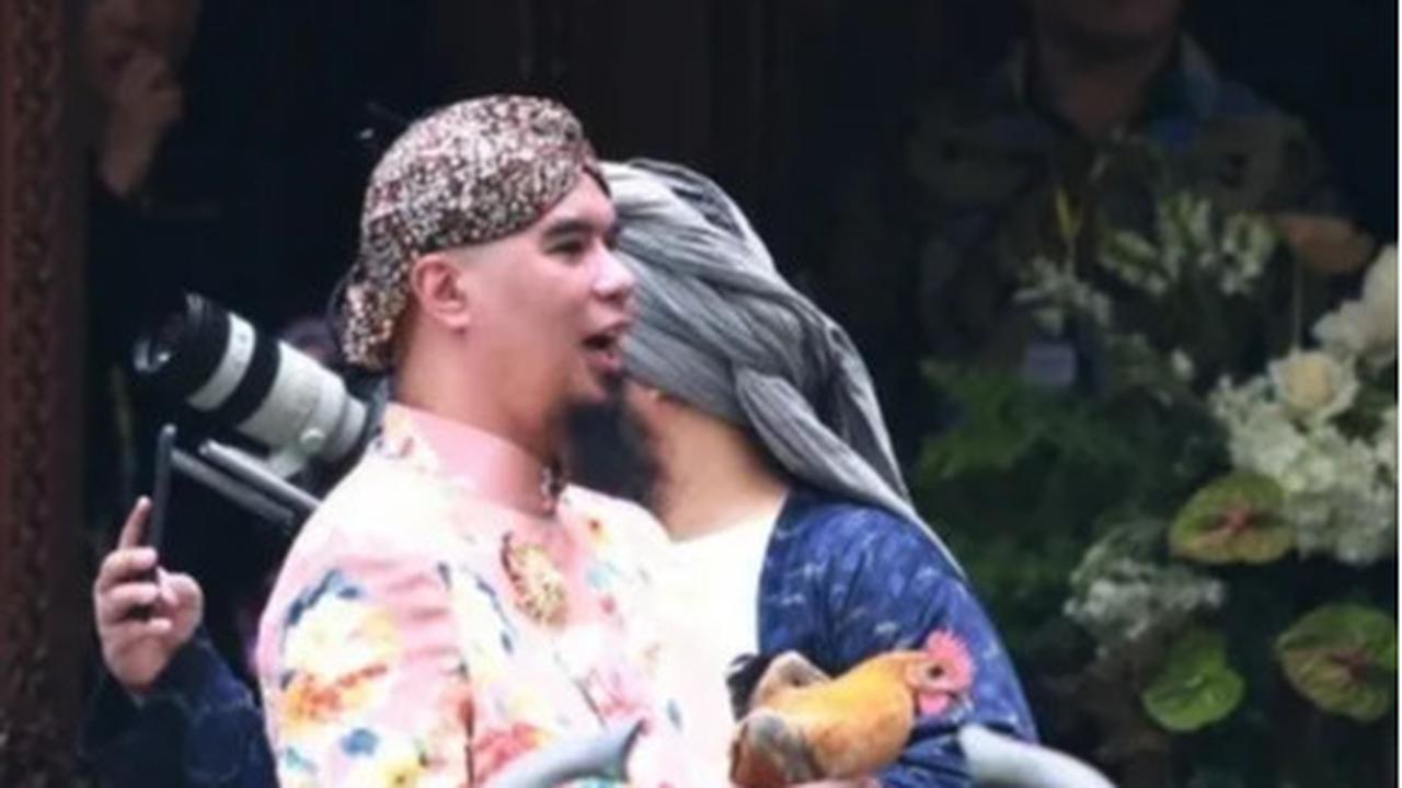Mengenakan beskap Jawa warna cerah beserta blankon, Ahmad Dhani tampak memegang ayam kampung dengan ekspresi bahagia.