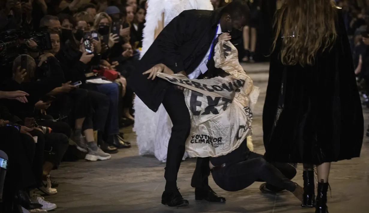 Pengunjuk rasa dikeluarkan dari runway peragaan busana Louis Vuitton Spring/Summer 2022 di Paris, Selasa (5/10/2021). Pengunjuk rasa itu berjalan di atas catwalk Paris Fashion Week dengan membawa spanduk yang mengutuk dampak konsumsi berlebihan terhadap lingkungan. (Vianney Le Caer/Invision/AP)