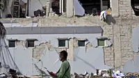 Seorang pria berjalan melewati bangunan yang rusak akibat gempa di Mamuju, Sulawesi Barat, Indonesia, Senin (18/1/2021). Jumlah warga yang mengungsi usai gempa magnitudo 6,2 di Sulawesi Barat mencapai 19.435 orang. (AP Photo/Yusuf Wahil)