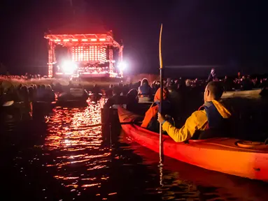 Para penonton menyaksikan penampilan band Dagamba dari atas perahu saat konser musik Laivā di Danau Juglas, Riga, Latvia, 14 Agustus 2021. Warga Latvia bisa menikmati konser musik dari atas kayak, sampan, dan kapal motor bahkan ketika mereka belum divaksin COVID-19. (Gints Ivuskans/AFP)