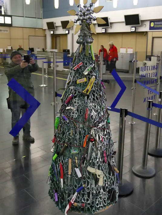 Seorang pria mengambil gambar Pohon Natal yang dirakit dari barang-barang sitaan di Bandara Vilnius, Lithuania pada 12 Desember 2019. Pohon Natal unik ini sekaligus untuk memperingatkan penumpang agar jangan membawa benda-benda terlarang. (Photo by Petras Malukas / AFP)