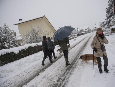 Orang-orang berjalan dengan anjing mereka di salju di Burguete, Spanyol utara, Senin, 16 Januari 2023. Pihak berwenang telah mengumumkan salju dan suhu sangat rendah selama beberapa hari ke depan di seluruh bagian utara negara itu. (AP Photo/Alvaro Barrientos)