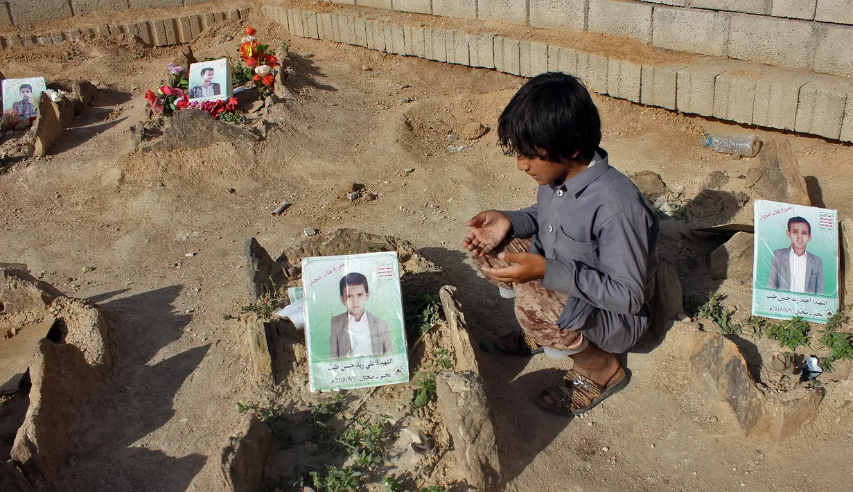 Seorang anak berdoa di makam anak-anak sekolah di sebuah pemakaman di provinsi kubu pemberontak Huthi di Saada (4/9). Anak-anak tersebut tewas terkena serangan udara koalisi pimpinan Saudi di pasar Dahyan pada bulan Agustus. (AFP Photo/Stringer)