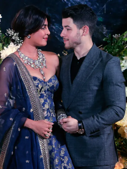 Pasangan aktris Bollywood Priyanka Chopra dan musisi Nick Jonas berpose untuk resepsi kedua pernikahan mereka di Mumbai, India, Rabu (19/12). Malam itu, Priyanka Chopra mengenakan gaun biru navy tanpa tali dengan sulaman emas. (AP/Rajanish Kakade)
