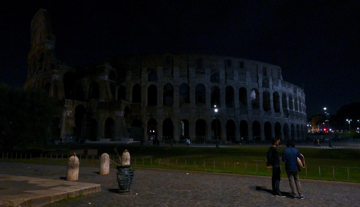 Para pejalan kaki berjalan di samping Colosseum kuno, dengan lampu-lampu monumen yang dipadamkan sebagai bagian dari inisiatif Earth Hour, di Roma pada tanggal 25 Maret 2023. - Earth Hour, yang dimulai di Australia pada tahun 2007, diikuti oleh jutaan pendukung di 187 negara, yang memadamkan lampu pada pukul 20.30 waktu setempat dalam apa yang disebut oleh penyelenggara sebagai "gerakan akar rumput terbesar di dunia untuk perubahan iklim". (Vincenzo PINTO / AFP)