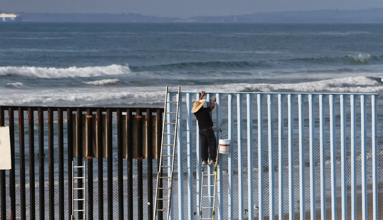 Seorang warga sedang mengecat pagar perbatasan antara Meksiko dan Amerika Serikat di Playas Tijuana, Meksiko (10/12). Pagar yang sebelumnya terlihat usang dan penuh karat nantinya akan diubah menjadi lebih berwarna. (Reuters/Jorge Duenes)