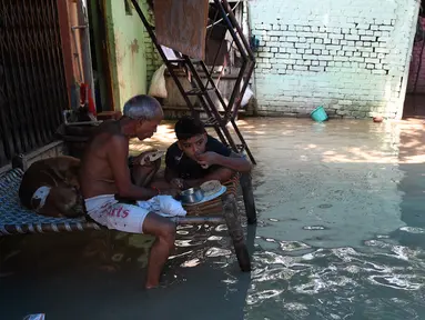 Seorang pria dan anak laki-laki makan di atas bangku saat banjir melanda daerah perumahan dekat tepi Sungai Yamuna yang meluap di New Delhi, India, Selasa (20/8/2019). (AFP Photo/Sajjad Hussain)