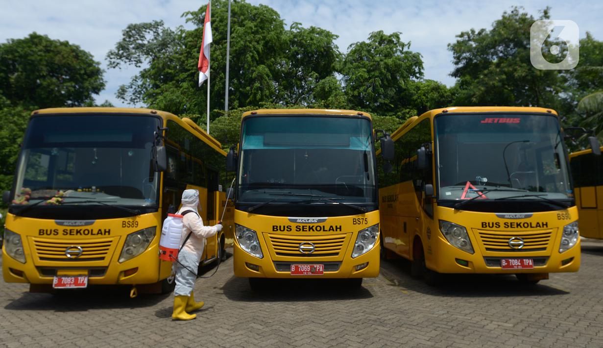 Petugas ber-APD menyemprotkan disinfektan pada bus sekolah di Posko Gabungan PSBB dan Gakplin Protkes, Puskesmas Jatinegara, Jakarta, (22/9/2020). Sejumlah unit bus sekolah kini dialihfungsikan menjadi kendaraan untuk mengantar pasien Covid-19 berstatus menuju Wisma Atlet. (merdeka.com/Imam Buhori)