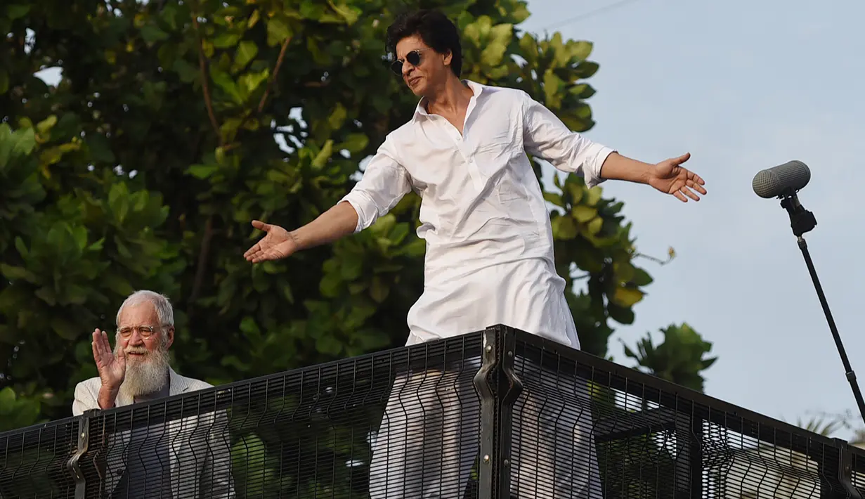 Aktor Bollywood, Shah Rukh Khan (kanan) disaksikan pembawa acara televisi AS, David Letterman menyapa para fans yang berkumpul di depan rumahnya pada perayaan Idul Fitri di Mumbai, Rabu (5/6/2019). Shah Rukh Khan tetap melakukan tradisi menyapa penggemar dari balkon atas rumahnya (SUJIT JAISWAL/AFP)