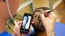 Menggunakan telepon genggam, Rob Ferrel, berusaha melukiskan wajah bintang sepak bola Meksiko, Javier Hernández Balcazar, di kepala pelanggannya di San Antonio, Texas, (30/6/2014). (REUTERS/Ashley Landis)