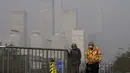 Sepasang suami istri yang mengenakan masker untuk membantu mengekang penyebaran virus corona berjalan di jembatan di atas gedung perkantoran di Kawasan Pusat Bisnis yang diselimuti kabut polusi di Beijing, Kamis (18/11/2021).  (AP Photo/Andy Wong)