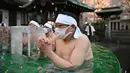 Penganut Shinto dari Kuil Teppozu Inari mandi dengan air dingin untuk mensucikan jiwa dan tubuh mereka selama ritual Tahun Baru di Tokyo, Jepang, Minggu (9/1/2022). Beberapa orang lalu ada yang terlihat memeluk es batu yang disediakan di bak tersebut. (Philip FONG/AFP)