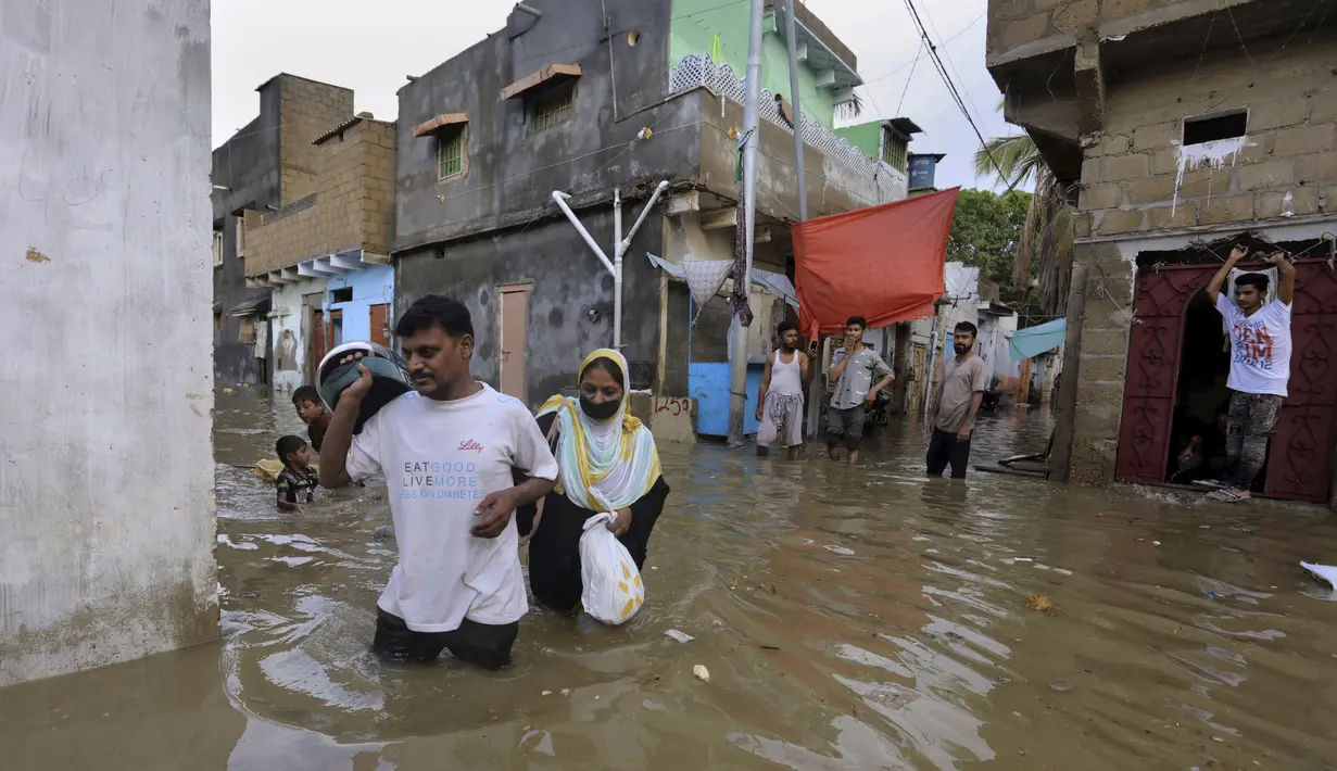 Warga melintasi jalan banjir setelah hujan deras di Karachi, Pakistan, Minggu, (26/7/2020). Sebagian warga memilih untuk bertahan meski rumah mereka terendam banjir. (AP Photo/Fareed Khan)