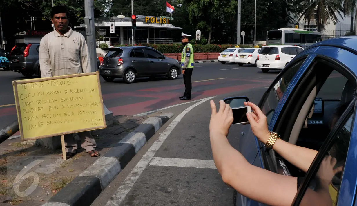 Penumpang taksi mengabadikan aksi Syaripudin Dodo (59) di Bundaran HI, Jakarta, Kamis (30/7/2015). Kakek ini meminta pertolongan pengguna jalan untuk membiayai sekolah cucunya di Perguruan Islam Al Masthuriyah Sukabumi. (Liputan6.com/Johan Tallo)