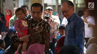 Presiden Joko Widodo (Jokowi) menggendong balita sambil mengajak Presiden Bank Dunia Jim Yong Kim blusukan ke Desa Tangkil, Kecamatan Caring, Bogor, Rabu (4/7). Keduanya meninjau Posyandu dan PAUD di dekat SDN 01 Tangkil. (Liputan6.com/Angga Yuniar)