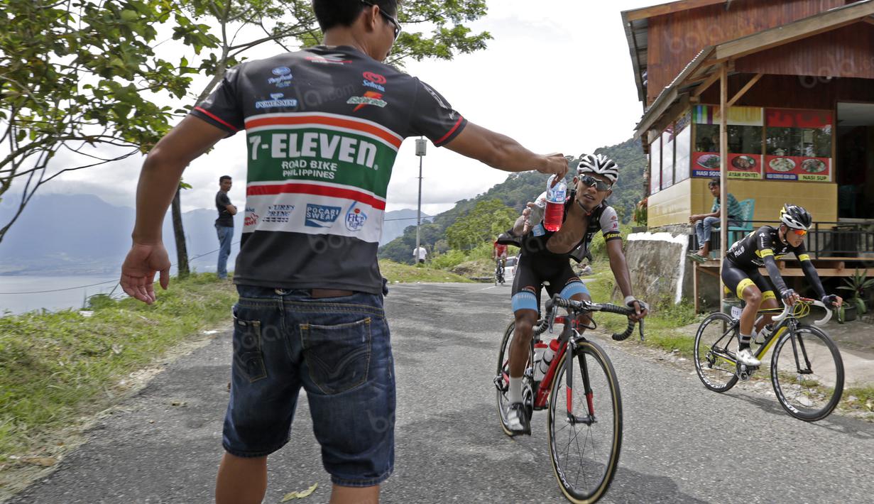 Seorang asisten tim memberikan minum kepada pebalap yang melintas jalur kelok 44  etape ke-4 Tour de Singkarak 2016 di Kabupaten Agam, Sumatera Barart. (Bola.com/NIcklas anoatubun)