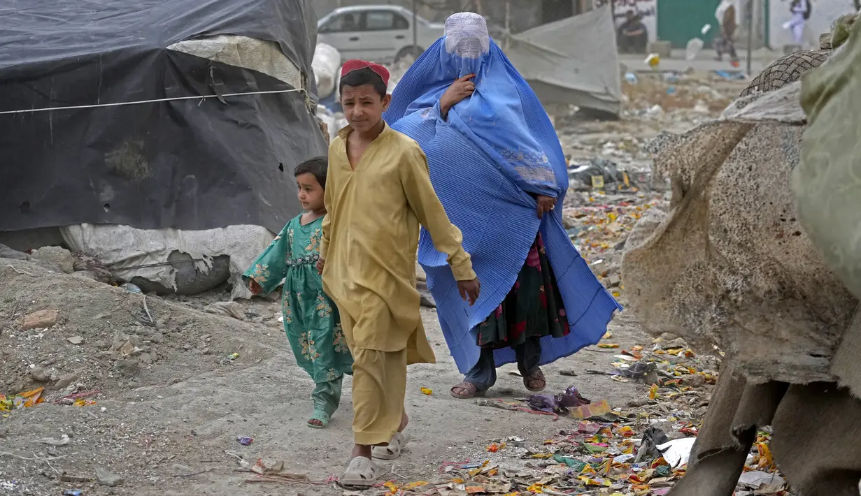 <p>Seorang perempuan yang mengenakan burqa dan anak-anaknya berjalan di depan rumah mereka di Kabul, Afghanistan, 8 Mei 2022. Taliban memerintahkan perempuan Afghanistan untuk mengenakan pakaian dari kepala hingga ujung kaki atau burqa tradisional di depan umum. (AP Photo/Ebrahim Noroozi)</p>