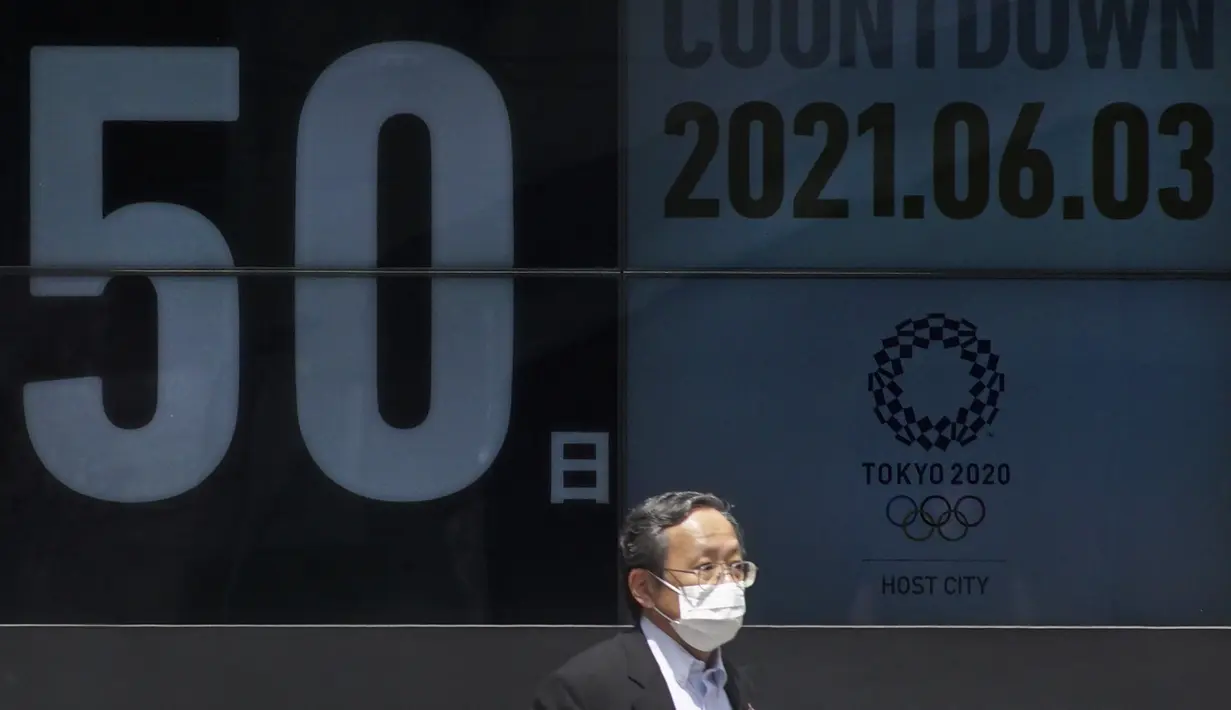 Seorang pria berjalan melewati papan hitung mundur untuk Olimpiade Tokyo 2020 50 hari sebelum upacara pembukaan, di Tokyo, Kamis (3/6/2021). (AFP/ Kazuhiro Nogi)
