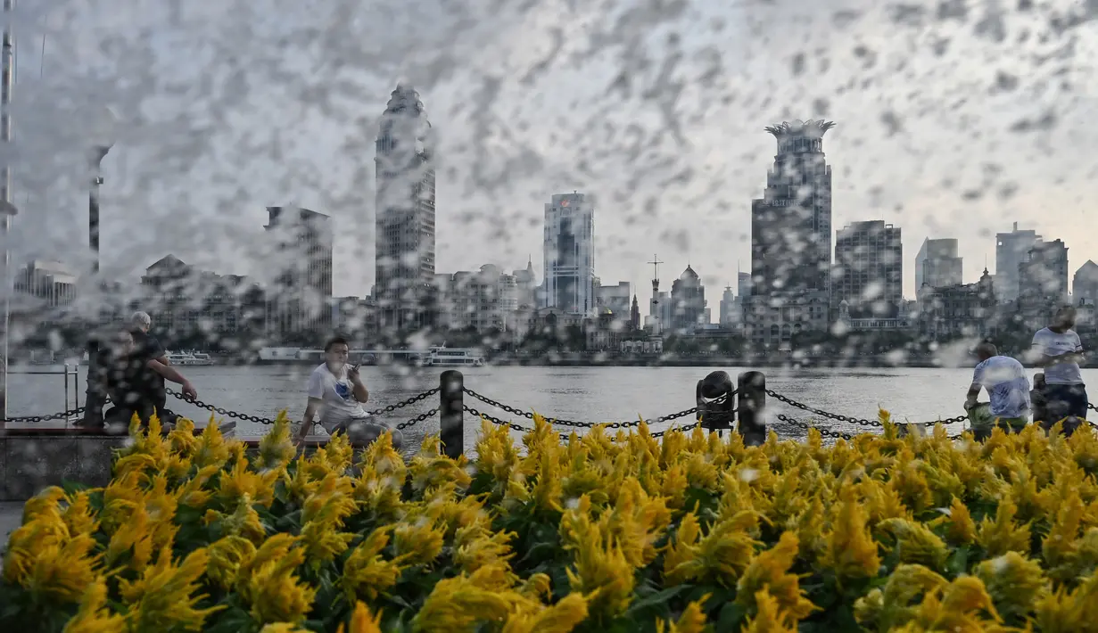 Warga duduk di sepanjang Sungai Huangpu saat petugas menyiramkan air ke tanaman di Shanghai (15/7/2019). Sungai Huangpu adalah sungai terbesar di Shanghai. Kawasan Bund di Distrik Huangpu di pusat Shanghai yang terkenal terletak di sepanjang sisi sungai. (AFP Photo/Hector Retamal)