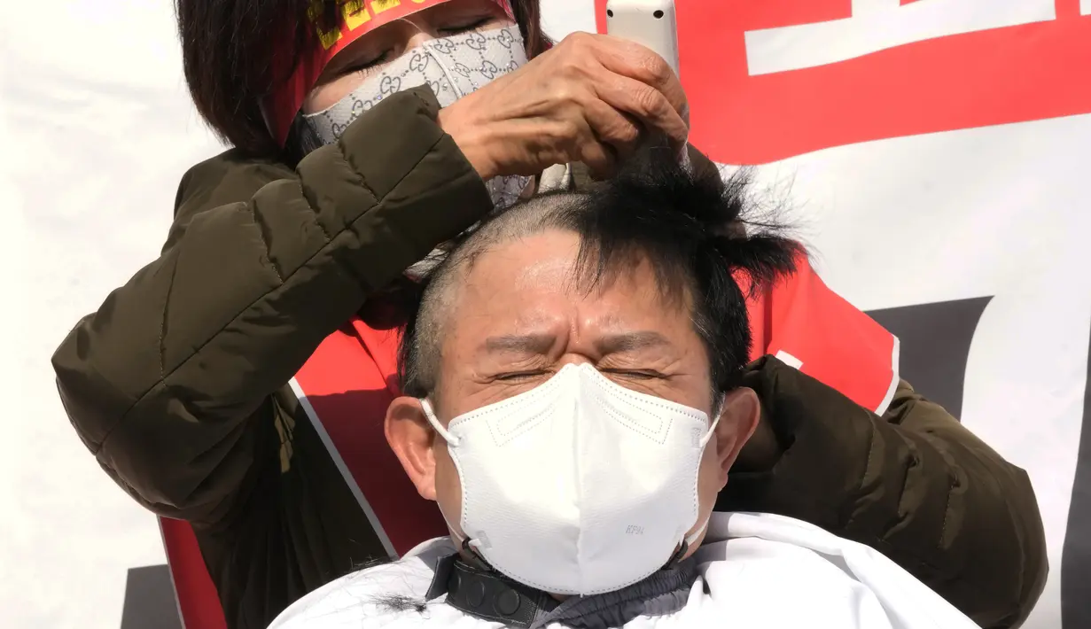 Seorang pemilik usaha kecil dicukur rambutnya saat unjuk rasa menentang aturan jarak sosial pemerintah di dekat Kompleks Pemerintah di Seoul, Korea Selatan, Selasa (15/2/2022). Korea Selatan melaporkan jumlah kematian COVID-19 tertinggi dalam sebulan Selasa (15/2). (AP Photo/Ahn Young-joon)