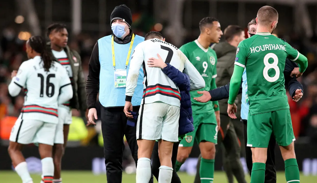 Seorang fans cilik memeluk striker Portugal Cristiano Ronaldo setelah berlari memasuki lapangan pada akhir laga Grup A Kualifikasi Piala Dunia 2022 Zona Eropa melawan Irlandia di Stadion Aviva, Jumat (12/11/2021) dinihari WIB. Fans itu nekat menerobos petugas keamanan stadion. (Paul Faith / AFP)