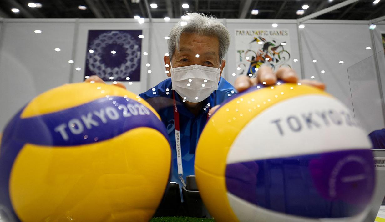 Seorang sukarelawan yang mengenakan masker sebagai tindakan pencegahan terhadap virus Covid-19 berpose dengan bola voli di belakang kaca pelindung di pusat media menjelang pembukaan Olimpiade Tokyo 2020 di Tokyo pada 20 Juli 2021. (AFP/Franck Fife)