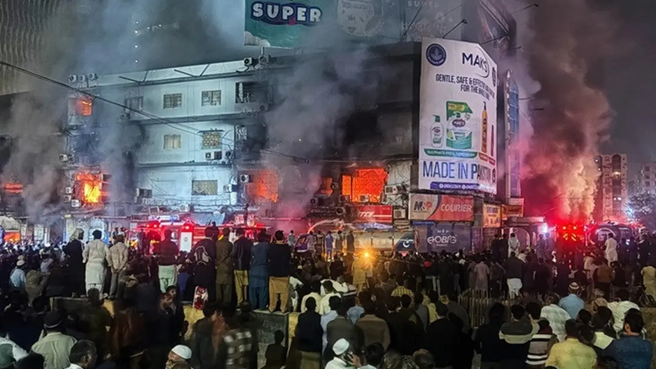 Warga berkumpul menyaksikan petugas pemadam kebakaran yang berupaya mengendalikan kebakaran besar di sebuah pusat perbelanjaan bertingkat di Karachi, Pakistan, Minggu (18/1/2026).