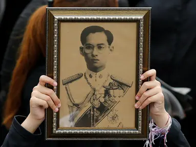 Seorang pelayat wanita memegang foto Raja Bhumibol Adulyadej saat berkumpul di luar Grand Palace sambil menyanyikan rekaman lagu kerajaan untuk menghormati raja mereka, di Bangkok, Thailand, (22/10) (REUTERS/Jorge Silva)