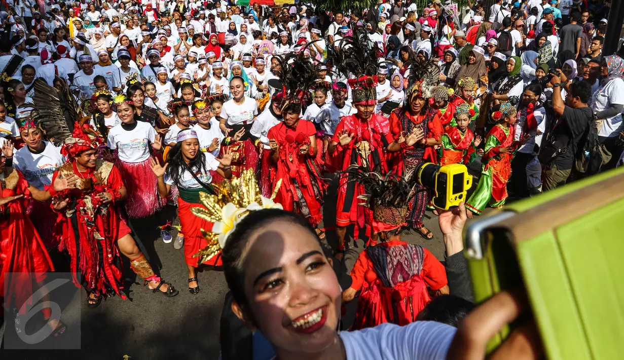 Seorang peserta mengambil gambar dengan latar belakang flashmob 1745 penari di kawasan Senayan Jakarta, Minggu (21/8). Kegiatan bertajuk "Aku Indonesia-Bagimu Negeri Kami Menari" itu merupakan bagian dari perayaan HUT RI ke 71. (Liputan6.com/Fery Pradolo)