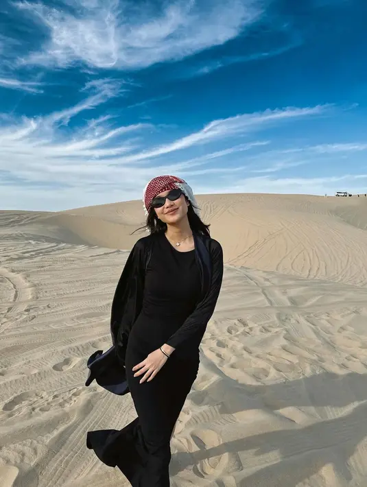 Kunjungi padang pasir di Qatar, istri Pratama Arhan, Azizah tampil kece dengan dress hitam dan sorban di kepalanya.