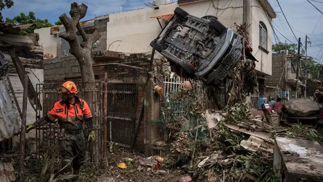 Seorang relawan penyelamat dari kelompok Topos terlihat di dekat sebuah mobil yang tersangkut di pagar di samping rumah rusak di Poza Rica, Meksiko, Senin (13/10/2025), setelah hujan deras mengguyur daerah itu.