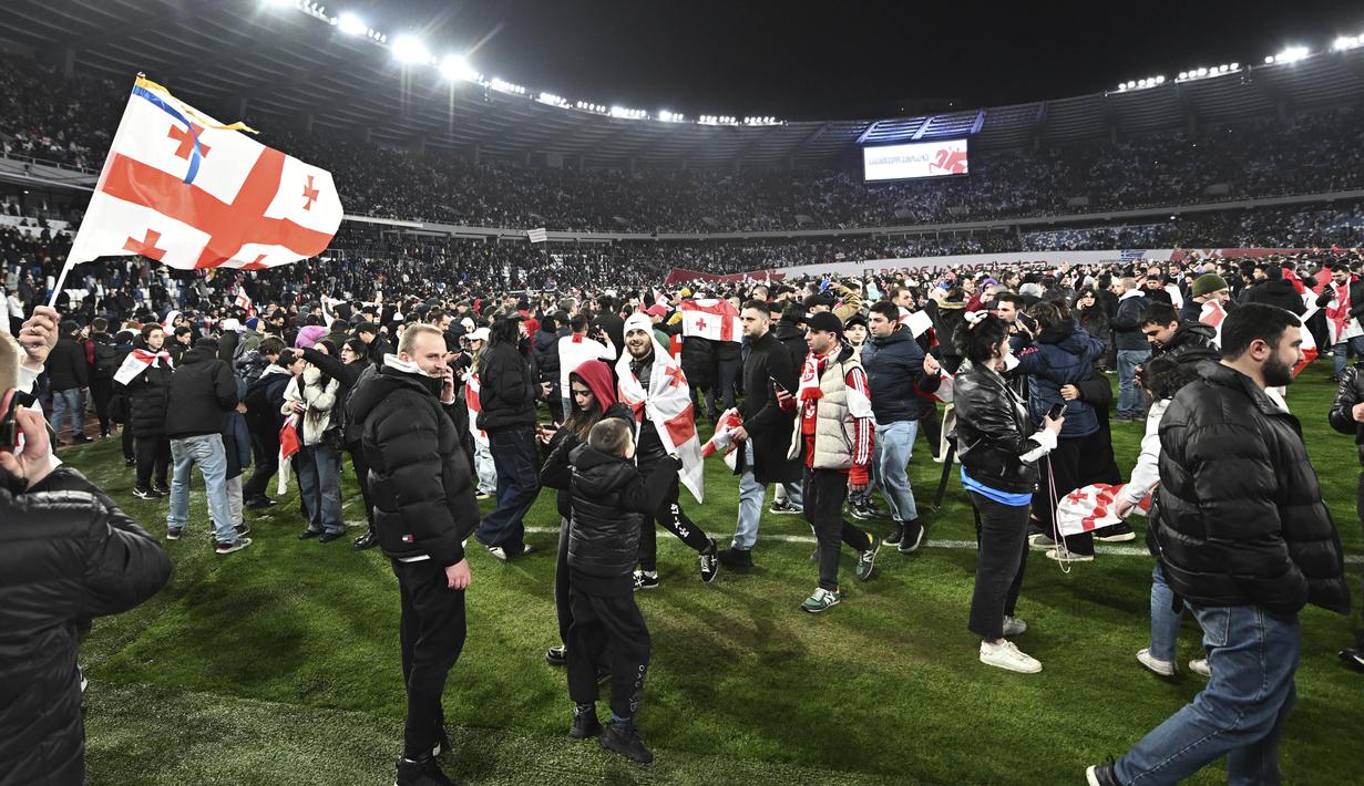 Suporter Timnas Georgia tumpah ruah turun kelapangan setelah timnya berhasil mengalahkan Yunani dalam laga playoff yang menegangkan di Tbilisi, Rabu (27/4/2024). Georgia sukses mencetak sejarah dengan lolos ke Euro 2024 untuk pertama kalinya. (AP Photo/Tamuna Kulumbegashvili)