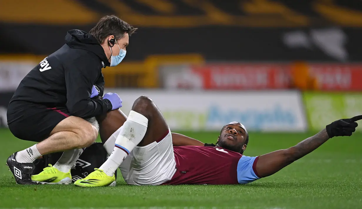Gelandang West Ham United, Michail Antonio mendapat perawatan usai mengalami cedera saat menghadapi Wolverhampton Wanderers dalam laga lanjutan Liga Inggris 2020/2021 pekan ke-30 di Molineux Stadium, Senin (5/4/2021). West Ham menang 3-2 atas Wolverhampton. (AFP/Laurence Griffiths/Pool)