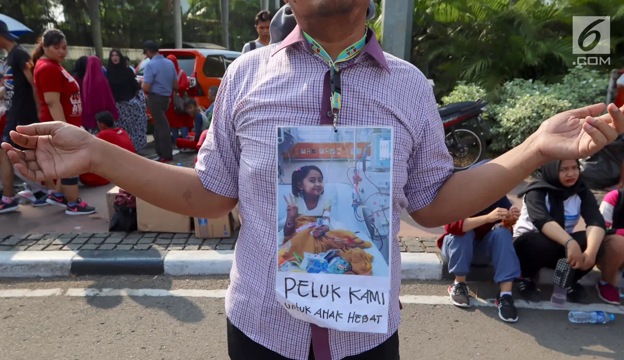 Seorang ayah mengalungkan foto anaknya saat melakukan Aksi Peduli Viara untuk biaya cuci darah dan cangkok ginjal di kawasan Bundaran HI, Jakarta, Minggu (10/09). Aksi memasuki minggu ke 5 saat Car Free Day. (Liputan6.com/Fery Pradolo)