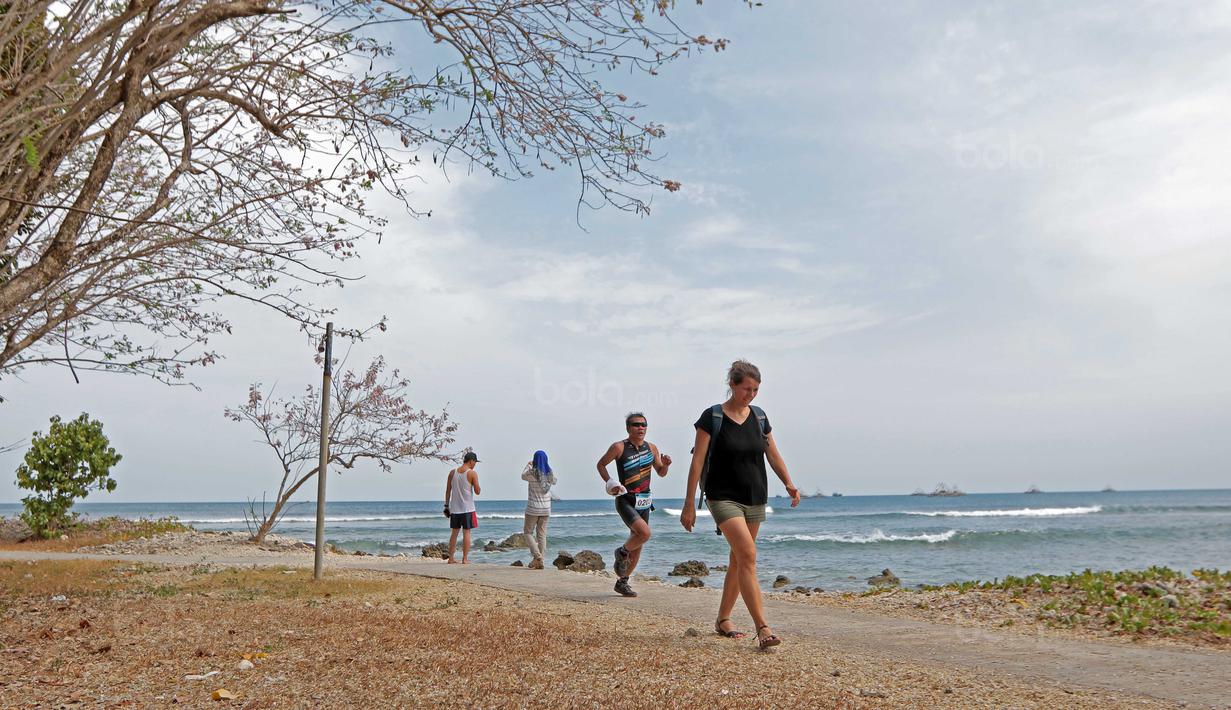 Seorang peserta (2kanan) Rhino Cross Triathlon melewati beberapa wisatawan dekat pantai pada Festival Pesona Tanjung Lesung 2017 di Tanjung Lesung, Banten (24/9/2017). Total jarak tempuh Rhino Cross Triathlon 38 km. (Bola.com/Nicklas Hanoatubun)