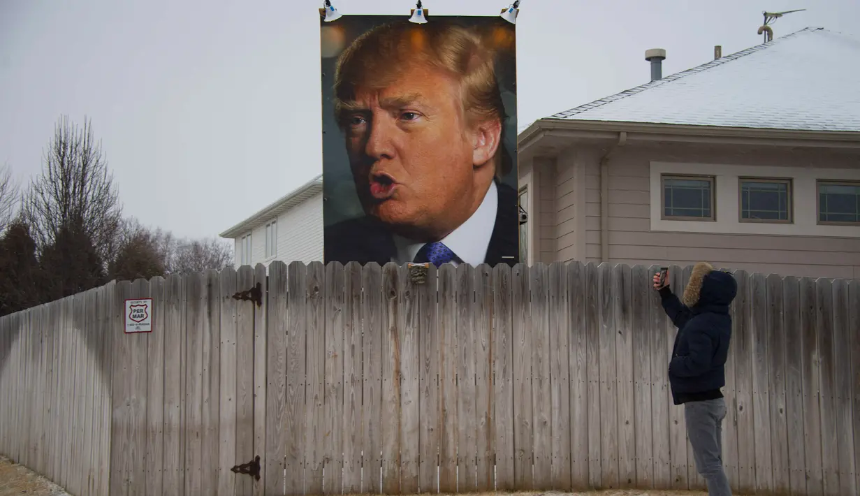 Seorang warga saat mengabadikan baliho besar calon Presiden AS Donald Trump dengan ponselnya di halaman belakang rumah George Davey di West Des Moines, Iowa, (25/1/2016). (AFP/JIM WATSON)