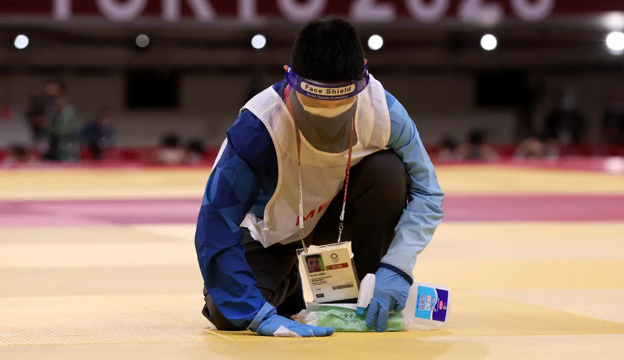 Seorang petugas membersihkan dan mendisinfektan matras pada pertandingan babak penyisihan -81kg judo putra antara Saeid Mollaei dari Mongolia dan Murad Fatiyev dari Azerbaijan selama Olimpiade Tokyo 2020 di Nippon Budokan di Tokyo pada 27 Juli 2021. (Jack GUEZ / AFP)
