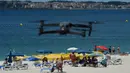 Sebuah drone atau pesawat tak berawak yang diterbangkan oleh polisi setempat memperingatkan orang-orang untuk menjaga jarak di pantai Areas di Sanxenxo, Spanyol, Selasa (14/7/2020). Drone tersebut untuk memantau jaga jarak antarwisatawan saat berlibur di masa pandemi Corona. (MIGUEL RIOPA / AFP)