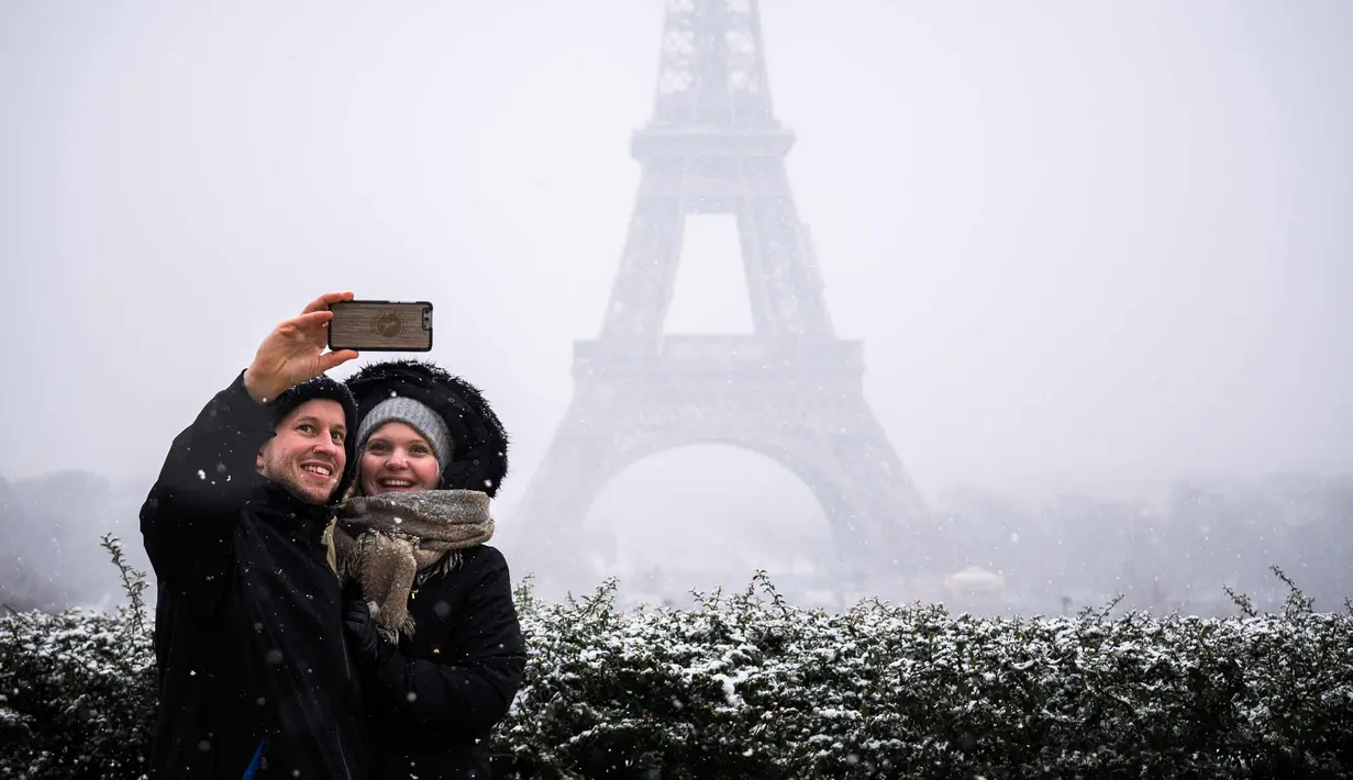 Pasangan berselfie di depan Menara Eiffel di Paris, Prancis (5/2). Ratusan orang terpaksa meninggalkan mobil mereka untuk tidur di tempat penampungan darurat akibat cuaca ekstrem yang melanda. (AFP Photo/Lionel Bonaventure)