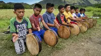 Sejumlah anak laki-laki memainkan rebana tradisional saat mengambil bagian dalam tari Rapa'i Geleng di sepanjang sawah di desa ekowisata Nusa, Lhoknga, Provinsi Aceh, 26 September 2021. Rapa'i Geleng adalah tarian yang berasal dari Aceh bagian selatan tepatnya Manggeng. (CHAIDEER MAHYUDDIN/AFP)