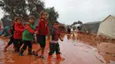 Anak-anak berjalan melewati genangan air hujan di depan tenda di sebuah kamp untuk warga Suriah yang kebanjiran di dekat desa Killi di utara provinsi Idlib barat laut (5/12/2019). (AFP Photo/Aaref Watad)