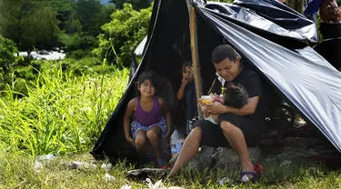 Seorang ayah memberi susu botol jus jeruk kepada putrinya yang masih bayi di tepi Sungai Huixtla, negara bagian Chiapas, Meksiko, Rabu (8/5/2022). Keluarga itu adalah rombongan dari kelompok migran, banyak dari Amerika Tengah dan Venezuela, yang meninggalkan Tapachula. (AP Photo/Marco Ugarte)