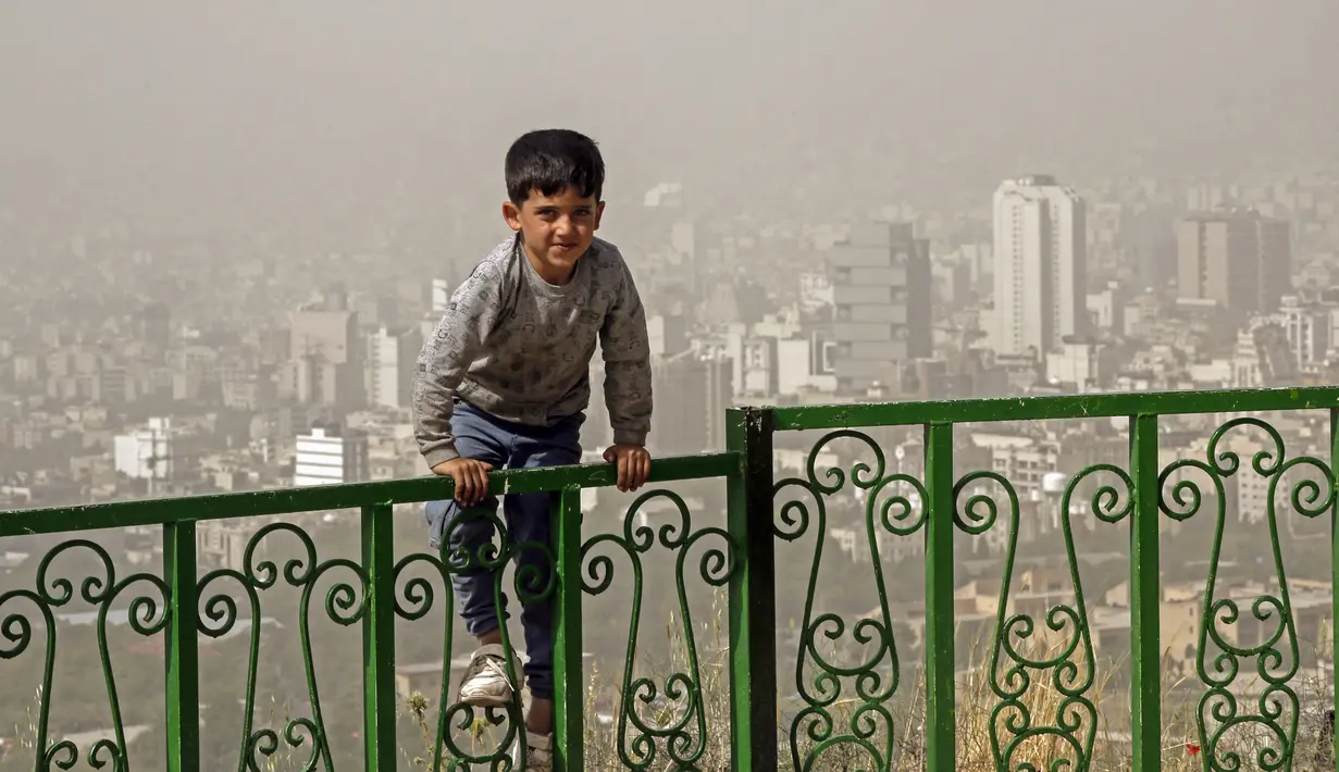 Seorang anak laki-laki bermain di luar selama badai pasir besar di utara ibu kota Iran, Teheran pada 17 Mei 2022. Kantor-kantor pemerintah, serta sekolah dan universitas diumumkan ditutup di banyak provinsi di Iran karena kondisi "cuaca tidak sehat" dan badai pasir yang menyelimuti, menurut laporan media pemerintah. (AFP)