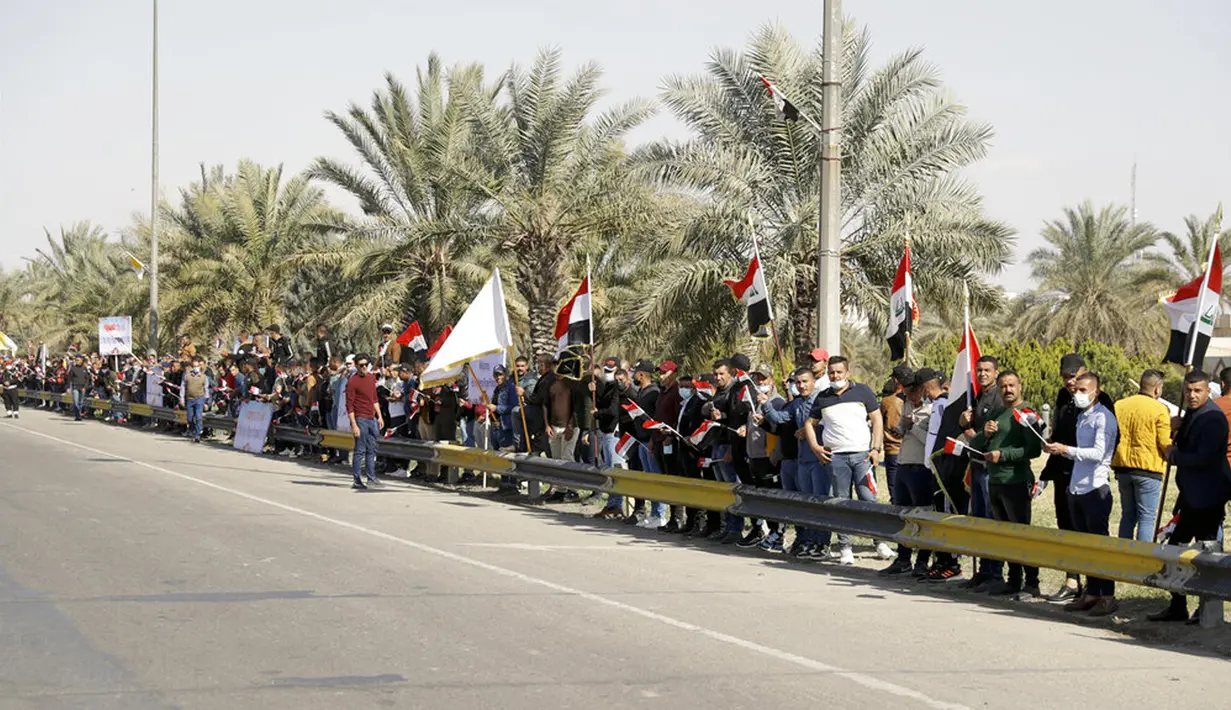 Orang-orang berdiri di pinggir jalan saat mereka menunggu Paus Fransiskus tiba di Baghdad, Irak, Jumat (5/3/2021). Paus Fransiskus datang ke Irak untuk mendesak umat Kristen tetap tinggal dan membantu membangun kembali Irak setelah bertahun-tahun perang. (AP Photo/Andrew Medichini)