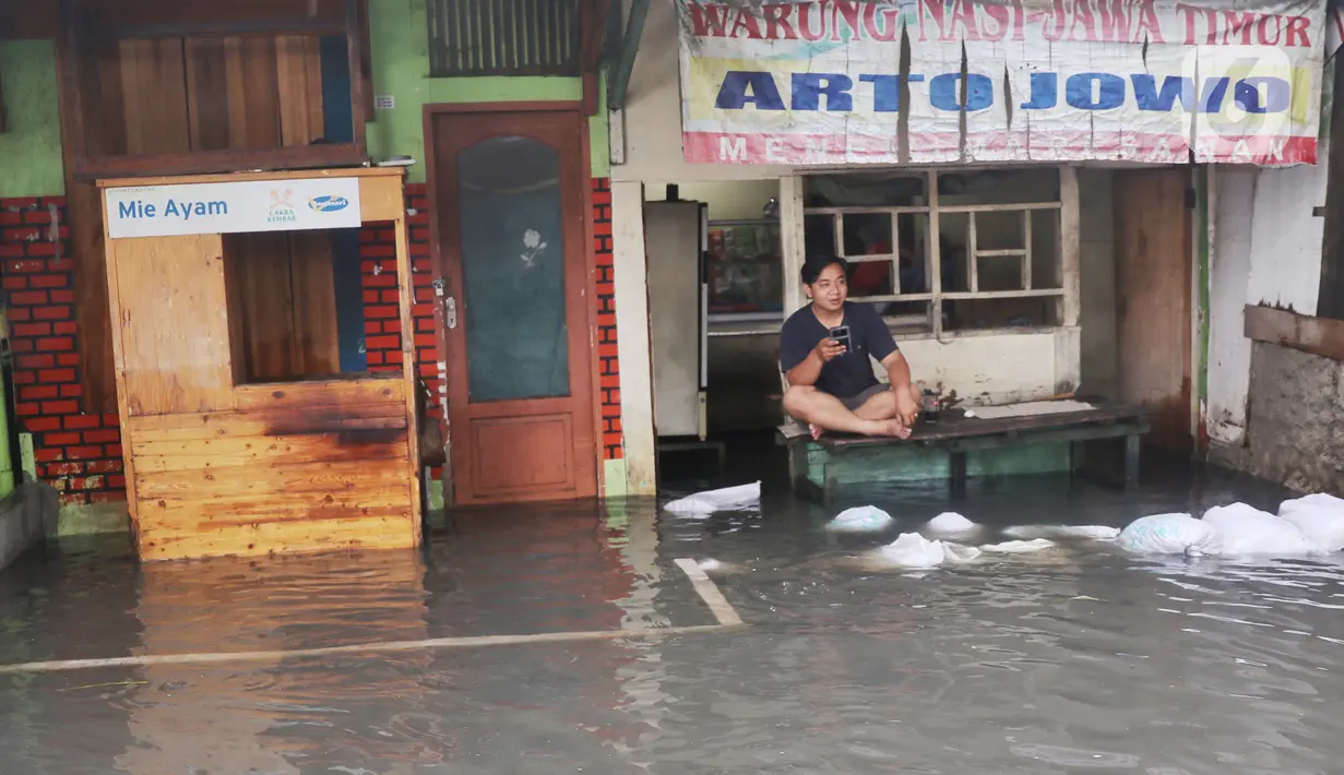 Seorang pria duduk di depan warung yang terendam banjir di Jalan KH. Ahmad Dahlan Cipondoh, Tangerang, Selasa (16/2/2021). Hujan deras yang melanda wilayah Tangerang mengakibatkan ruas jalan alternatif penghubung Tangerang - Jakarta itu banjir setinggi lutut orang dewasa (Liputan6.com/Angga Yuniar)